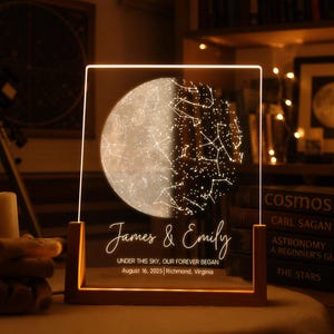 Peut inclure: Un panneau lumineux rectangulaire en acrylique avec un graphique brillant de lune et de constellations. Le texte indique James & Emily, UNDER THIS SKY, OUR FOREVER BEGAN, August 16, 2025, Richmond, Virginia. Le panneau est sur un socle en bois.