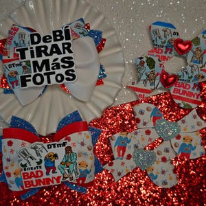 May include: Hair bows in red, white, and blue with glitter accents. Some bows feature the text "DeBi TIRAR MÁS FOTOS" and "BAD BUNNY". The bows have a cartoon illustration.