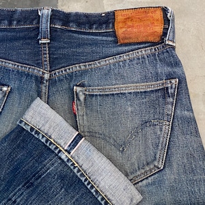 May include: Close-up of the back of blue denim jeans. The jeans have a classic five-pocket design, with a small red tag on the back pocket. The Levi Strauss & Co. leather patch is visible. The cuffs are rolled up, revealing the selvedge.