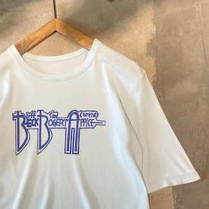 Puede incluir: Una camiseta de manga corta de color azul claro con un estampado gráfico morado en el pecho. El diseño muestra el texto Jeff Beck, Tim Bogert y Carmine Appice dispuesto en un formato lineal estilizado que recuerda a un instrumento técnico.