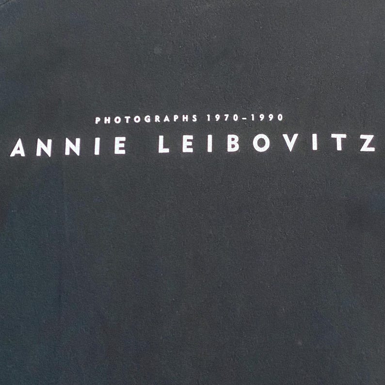 Może przedstawiać: Ciemnoszara okładka książki z białym napisem "ANNIE LEIBOVITZ". Nad imieniem znajduje się napis "PHOTOGRAPHS 1970-1990", r&oacute;wnież w kolorze białym. Tło jest jednolite, teksturowane i ciemnoszare.