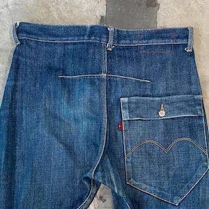 Puede incluir: Primer plano de la parte trasera de unos vaqueros azules. Los vaqueros tienen un diseño de bolsillo único con un contorno en forma de corazón y una pequeña etiqueta roja. Las costuras son visibles y la mezclilla tiene un aspecto desgastado.