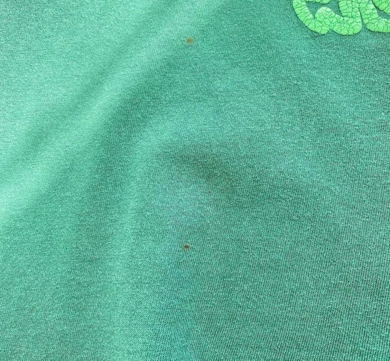 May include: Close-up of a teal green fabric with a textured surface. The fabric has a few small brown spots. A light green, textured design is visible in the upper right corner.
