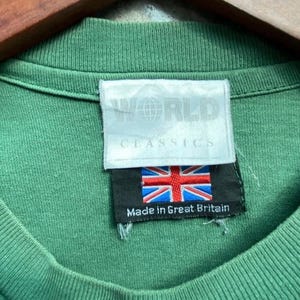 May include: Close-up of a green t-shirt collar with a tag that reads "WORLD CLASSICS." The tag also features the Union Jack flag and the text "Made in Great Britain."