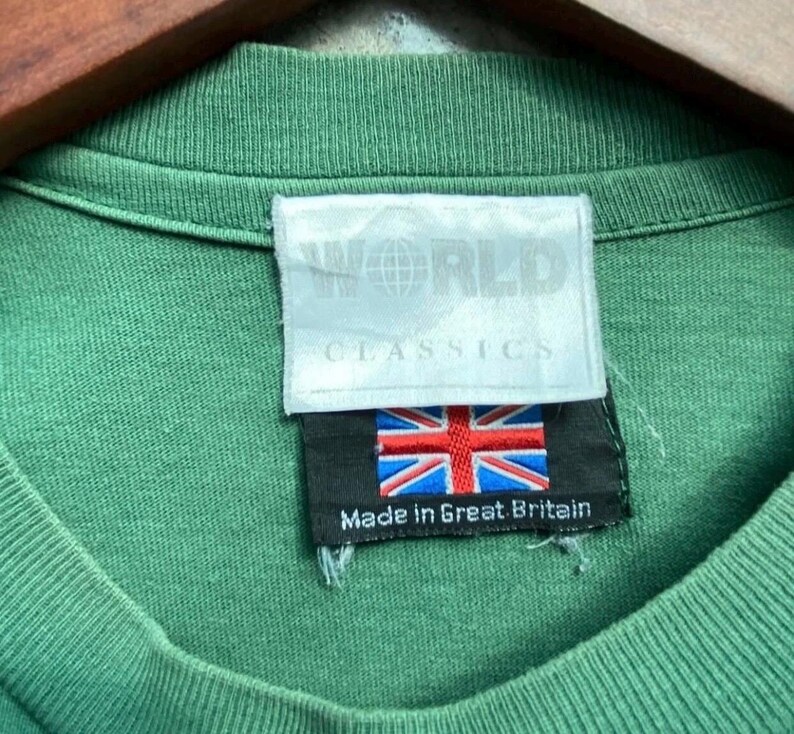 May include: Close-up of a green t-shirt collar with a tag that reads "WORLD CLASSICS." The tag also features the Union Jack flag and the text "Made in Great Britain."