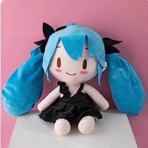 May include: A plush doll with a light blue hairstyle and black accents. The doll has a white face with brown eyes and rosy cheeks. It wears a black dress and has white arms and legs. The doll is a soft toy.