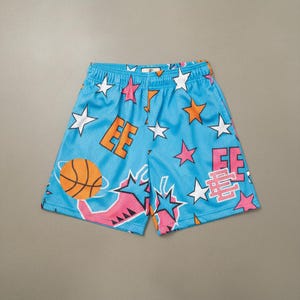 Può includere: Pantaloncini da basket in rete blu chiaro con un motivo di stelle, palloni da basket e le lettere "EE" in arancione e rosa. I pantaloncini hanno un girovita con coulisse e una vestibilità ampia.