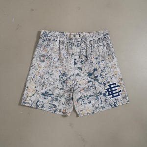 以下が含まれることがあります： 白と青の模様のショートパンツ、ウエストはゴム入り。 右下の脚にはネイビーブルーのロゴが付いています。 パターンには、青、黄、白の色合いが含まれています。