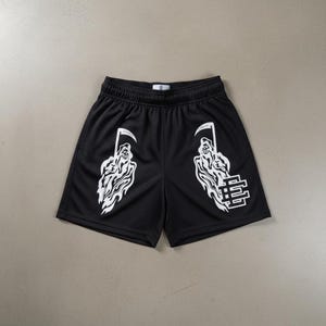 Könnte beinhalten: Schwarze Mesh-Shorts mit weißen Grafiken eines Sensenmanns, der eine Sense hält. Auf einem Bein befindet sich ein weißes "E" und "S" Logo. Die Shorts haben einen elastischen Bund.