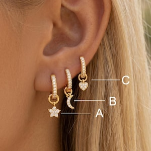 May include: Three gold hoop earrings with pavé-set clear stones. Each hoop features a dangling charm: A is a star, B is a crescent moon, and C is a heart. The earrings are labeled with white letters A, B, and C pointing to each specific charm.