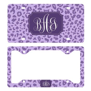 May include: A purple license plate and matching frame featuring a leopard print pattern. The license plate has a dark purple rectangular area with the initials "BHS" in white script. The frame has the same pattern and initials.