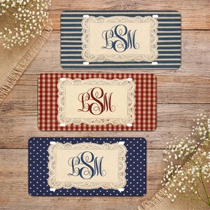 May include: Three decorative license plates with personalized initials. One plate has blue and white stripes, another has a red and white gingham pattern, and the third has a navy blue polka dot design. Each plate features a cream-colored frame with a lace design and the initials "LSM".