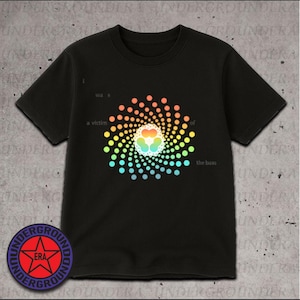 May include: Black t-shirt featuring a colorful spiral design with the text "I was a victim of the bass." The design includes a heart-shaped element at the center. A circular logo with text and a star is at the bottom.