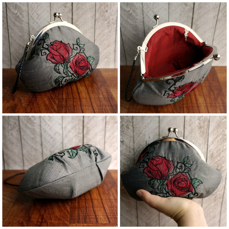 May include: A grey fabric coin purse with a silver clasp and embroidered red roses. The purse is open to reveal a red satin lining.
