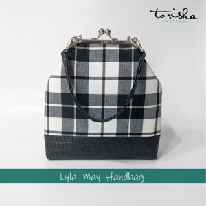 Puede incluir: Un bolso de mano de cuadros blanco y negro con una base de piel sint&eacute;tica negra. El bolso tiene un cierre de plata y una correa de cuero negro. El bolso est&aacute; etiquetado como "Lyla May Handbag".