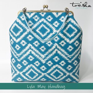 Puede incluir: Un bolso de mano de color azul turquesa y blanco con estampado, con una correa azul claro y un cierre de lat&oacute;n. El bolso de mano tiene un dise&ntilde;o geom&eacute;trico y el texto "Lyla May Handbag" est&aacute; impreso debajo de la imagen.