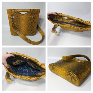 May include: A yellow snakeskin-patterned handbag with a top handle and a long shoulder strap. The bag has a zipper closure and a blue and white patterned lining.