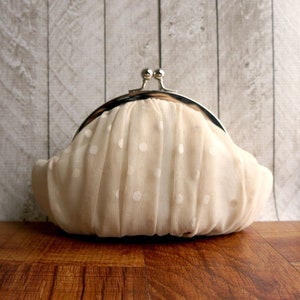 May include: A white polka dot clutch bag with a silver clasp. The bag is made of a soft, delicate fabric.