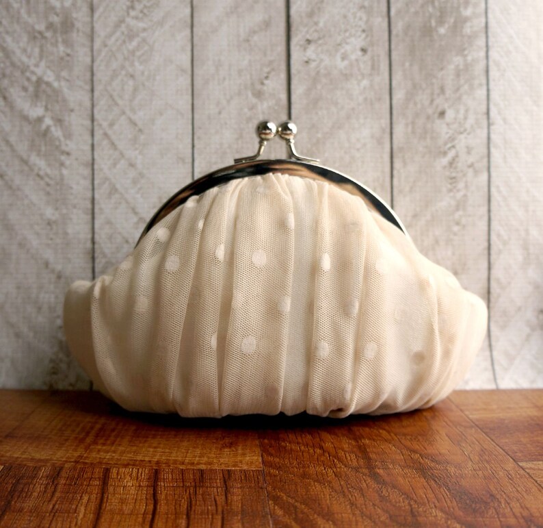 May include: A white polka dot clutch bag with a silver clasp. The bag is made of a soft, delicate fabric.