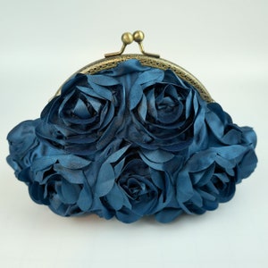 May include: A dark blue satin clutch bag with a gold metal frame and a floral design. The bag is made of fabric roses.