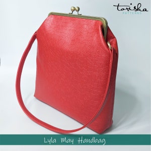 Puede incluir: Un bolso de mano rojo con cierre de broche y una correa larga. El bolso tiene un patr&oacute;n texturizado y en relieve. El texto "Lyla May Handbag" est&aacute; impreso debajo del bolso.