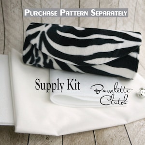 May include: A white fabric supply kit for a Barrette Clutch. The kit includes white fabric and a white interfacing. The text "Supply Kit" and "Barrette Clutch" is printed on the fabric.
