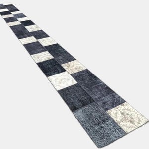 May include: A long, rectangular rug with a patchwork design. The rug features alternating sections of dark blue, off-white, and patterned beige squares. The rug is likely made of a woven material and is suitable for a hallway or entryway.