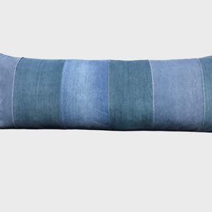 Könnte beinhalten: Ein langes, rechteckiges Zierkissen mit einem Patchwork-Design. Das Kissen hat vertikale Bahnen aus verschiedenfarbigem Jeansstoff in Blau, wodurch eine strukturierte Oberfläche entsteht. Das Kissen ist für die Inneneinrichtung konzipiert.
