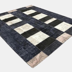May include: A rectangular area rug with a patchwork design. The rug features alternating stripes of black, white, and navy blue. The border is navy blue, and the corners have a patterned design in shades of beige and pink.