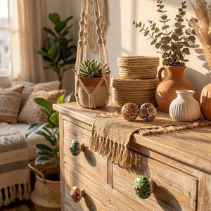 以下が含まれることがあります： 装飾的なノブ、吊り下げられた植物、さまざまな家の装飾品を備えた木製のドレッサー。 ドレッサーは天然木仕上げで、カラフルなノブが付いています。 マクラメのプラントハンガーには鉢植えの多肉植物が入っています。 織りのバスケットと花瓶も展示されています。