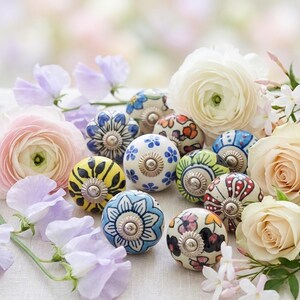 以下が含まれることがあります： 青、黄色、赤など、さまざまな色の花柄が施された装飾的なセラミックキャビネットノブのコレクション。パステルカラーの花々の間にノブが配置されています。
