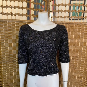 May include: A black sequined top with a floral design. The top has a scoop neckline and three-quarter sleeves.