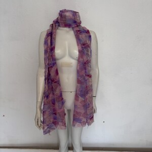 May include: A pink and purple patterned scarf with a frayed edge. The scarf is draped over a mannequin.