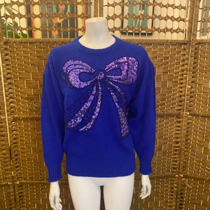 May include: A royal blue sweater with a large purple sequined bow on the front.