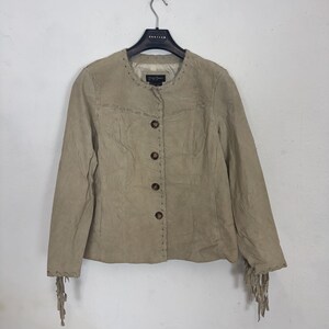 May include: A beige suede jacket with a round collar and button fastening. The jacket has decorative stitching and fringing on the cuffs. The garment is suspended from a black hanger.