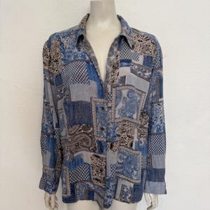 May include: A long-sleeved button-down shirt with a patchwork design in blue, grey, and beige. The shirt features paisley, checks, and geometric patterns. The shirt is displayed on a mannequin.