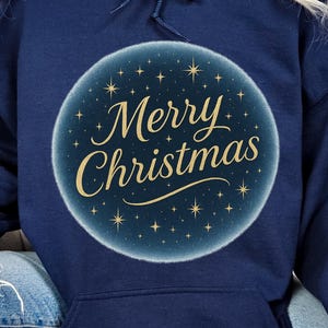 May include: Navy blue hooded sweatshirt featuring a circular design with the text "Merry Christmas" in gold script. The design is surrounded by small gold stars on a blue background. The sweatshirt has a front pocket.