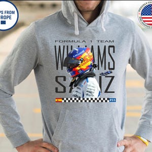 Może przedstawiać: Szara bluza z kapturem z motywem zespołu Formuły 1. Projekt zawiera kask kierowcy z numerem 55, nazwisko WILLIAMS i nazwisko SAIZ. Bluza ma przednią kieszeń i kaptur ze sznurkiem.