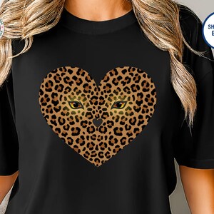 以下が含まれることがあります： 黒いTシャツ。ハート型のヒョウ柄のデザイン、金色の目、小さなハートが特徴です。Tシャツは半袖で、丸いネックラインです。デザインは前面の中央に配置されています。