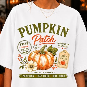 Könnte beinhalten: Ein weißes T-Shirt mit einer Grafik, die einen orangefarbenen Kürbis, grüne Blätter und den Text PUMPKIN Patch, FRESH FROM OUR FIELDS, GROWN WITH CARE, HAND PICKED, LOCALLY GROWN, PUMPKINS, HAY RIDES und HOT CIDER in Grün und Orange zeigt.
