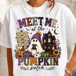 May include: A white t-shirt featuring a graphic with the text "MEET ME at the PUMPKIN patch". The design includes a ghost in a purple beanie holding a mug, a haunted house, pumpkins, and a wooden sign listing "HAY RIDES", "CARAMEL APPLES", "PUMPKINS", and "HOT CIDER".