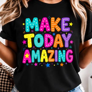 May include: A black t-shirt featuring the text "MAKE TODAY AMAZING" in large, multi-colored, patterned block letters. The design includes various decorative elements like dots, stripes, and squiggles, accented by small colorful stars and swirls.