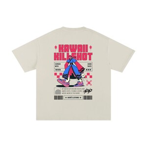 Puede incluir: Camiseta color crema con un diseño gráfico. El diseño presenta el texto "KAWAII KILL SHOT" en rosa y una figura de estilo anime. Se incluye texto adicional y elementos geométricos, con "AKIRO CLOTHING" en la parte inferior.