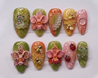 Può includere: Un set di dieci unghie finte a forma di mandorla con vari design. Le unghie presentano decorazioni 3D tra cui fiori, api, coccinelle e una rana. I colori includono verde, giallo, arancione e rosa, con accenti di goccioline d'acqua trasparenti.