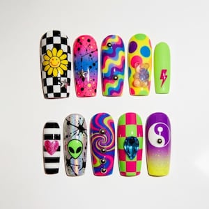 May include: A set of ten colorful press-on nails with various designs. The designs include a checkerboard pattern with a yellow daisy, a pink and blue splatter design, and a green alien.