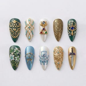 May include: A collection of ten artificial nails with various designs. The nails feature intricate embellishments in gold, teal, and white, with some showcasing floral patterns and geometric shapes. The designs include a sword, eye, and other decorative elements.