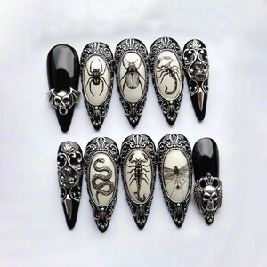 May include: A set of ten black and silver press-on nails. Each nail features a different design, including a spider, beetle, scorpion, snake, and dragonfly. The nails have a glossy finish and are adorned with ornate silver accents.
