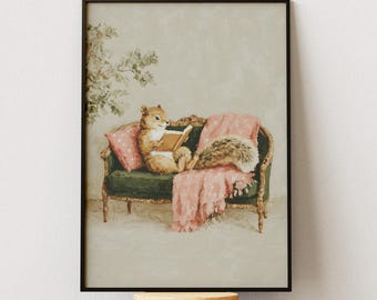 May include: A framed print depicts a fox reading on a green sofa with pink pillows and a blanket. The artwork is in a black frame and is displayed on a wooden and metal adjustable stool. The background is a light beige.