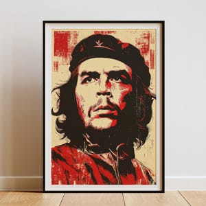 以下が含まれることがあります： ベレー帽をかぶった男性の様式化された肖像画が描かれた、額装されたアートプリント。アートワークは赤、黒、ベージュの色使いを使用しています。被写体は長い髪と真剣な表情をしています。プリントは黒いフレームに入っています。