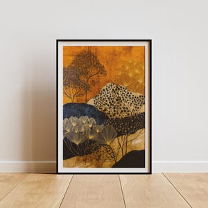 Op de afbeelding: Ingelijste kunstdruk met een abstract landschap met een gouden en oranje achtergrond. Het kunstwerk bevat gestileerde bomen, struiken en heuvels in zwart, marineblauw en goud. De print wordt gepresenteerd in een zwart frame en staat op een houten vloer.